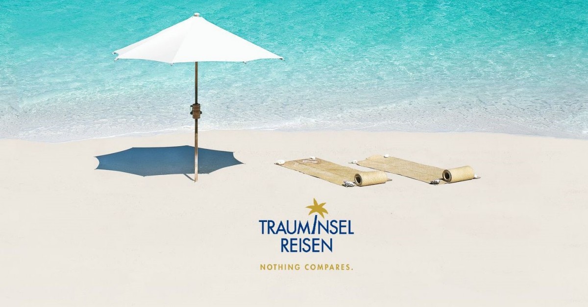 Ein Strand mit Sonnenschirm und liegen, auf dem Sand das Logo von Trauminsel Reisen