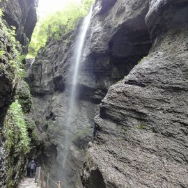 ein Wasserfall, links davon unten auf dem Weg hinten ein Wanderer
