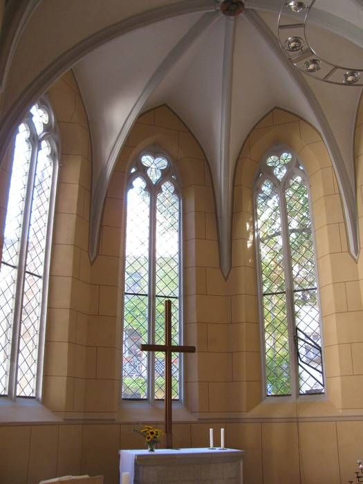 Der Innenraum mit heller Gotik-Gewölbedecke und gotischen Fenstern und Altar mit Kreuz.