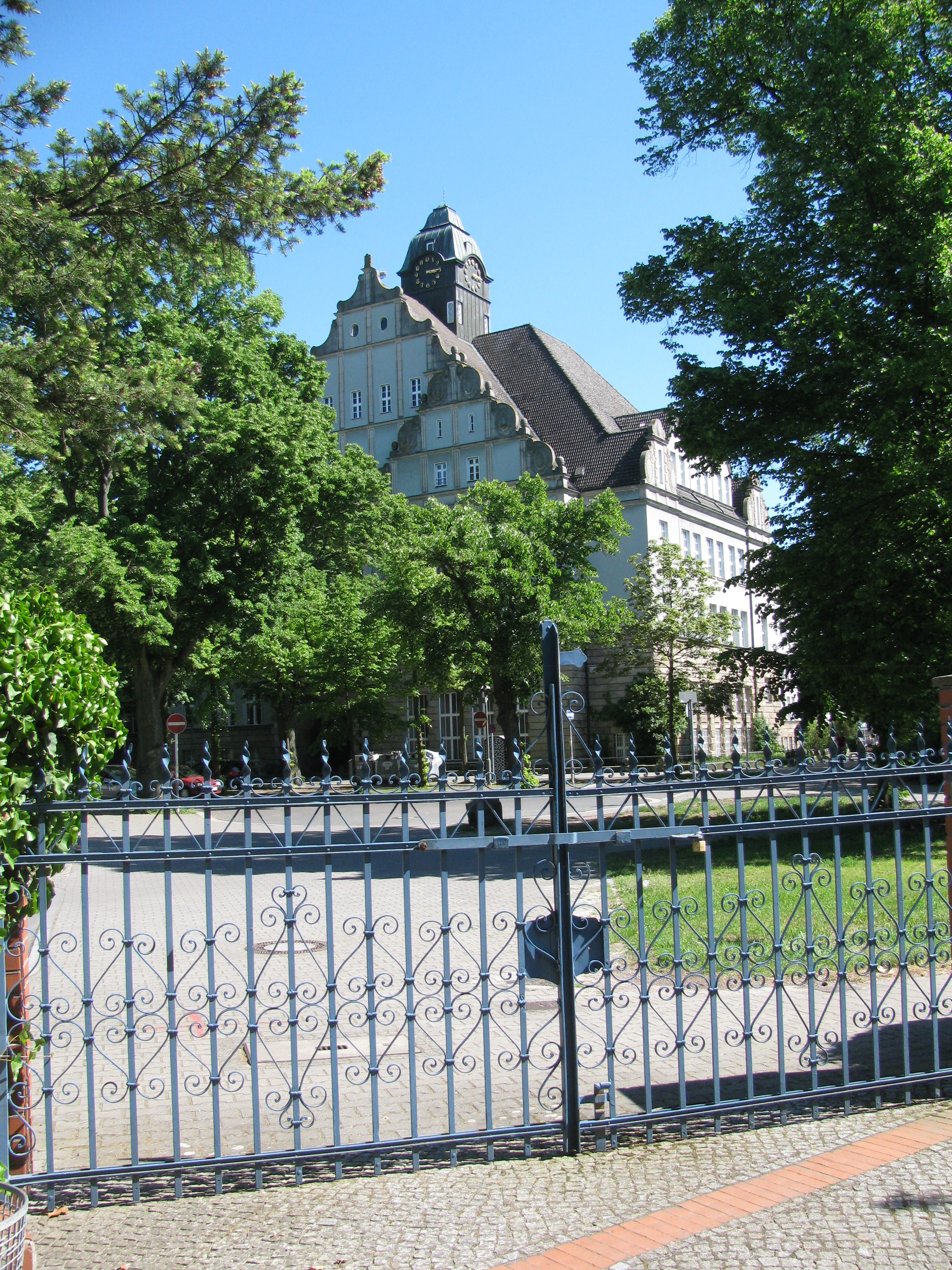 Humboldt-Gymnasium. Blick durch das schmiedeeiserne Eingangstor des Friedhofes Tegel vom Friedhof aus.