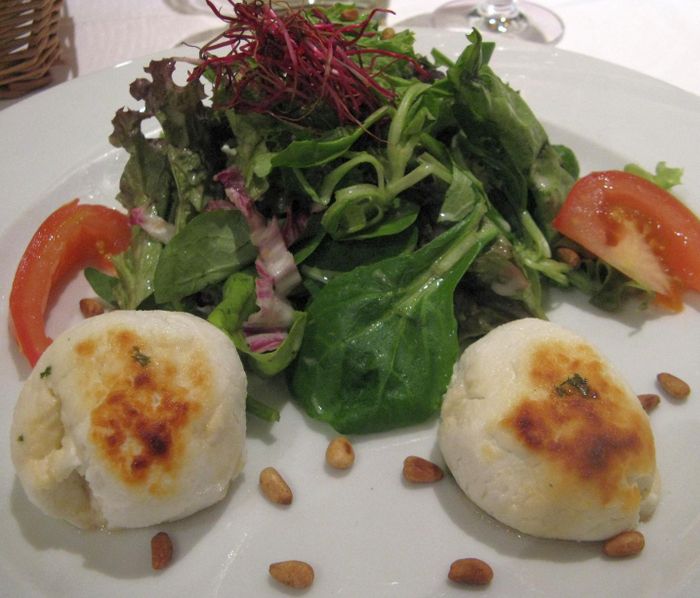 Warmer Ziegenfrischkäse, mit Thymian und Waldhonig glasiert, mit Salat und gerösteten Pinienkernen.