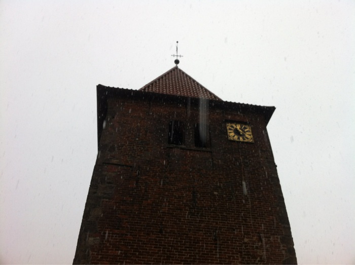 Schneeflocken am Kirchturm fallen aus dem grauen Himmel