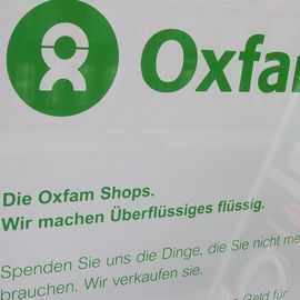 Plakat im Schaufenster vom Oxfam: wir machen &Uuml;berfl&uuml;ssiges fl&uuml;ssig- das Motto der Organisation