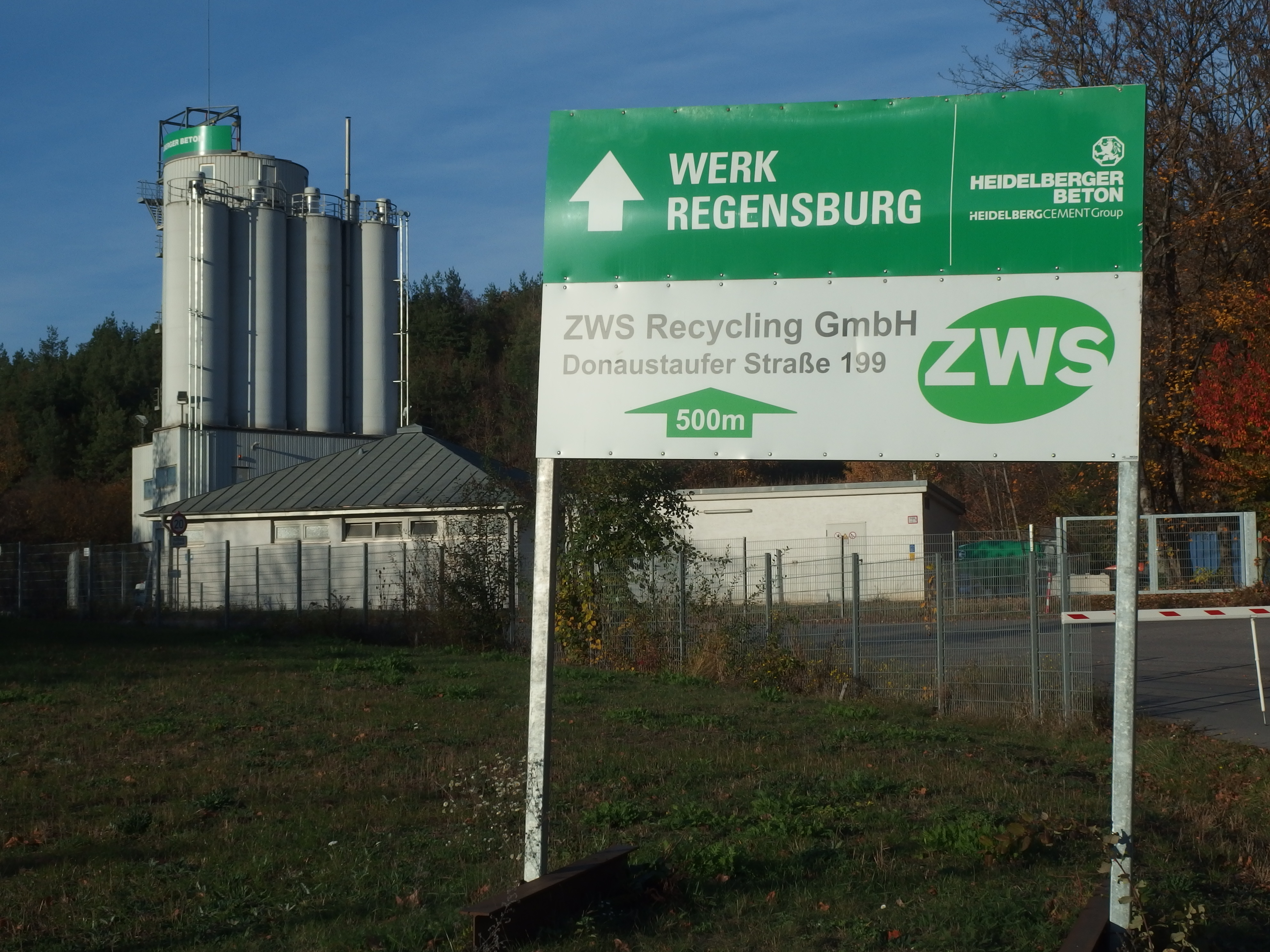 Tafel am Abzweig von der Straße + Produktionsanlagen dahinter