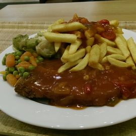 Schnitzel mit Pommes und darüber Zigeunersoße, dazu frisches Gemüse bestehend aus Erbsen, Möhren, Rosenkohl und Blumenkohl